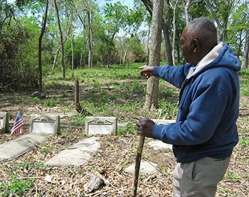 A man in a cemetery points toward the edge of bordering brush