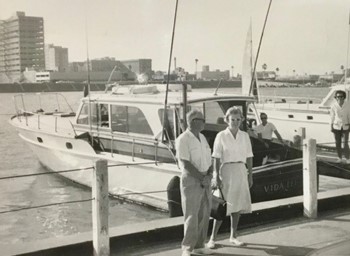A couple stands in front of a small yacht.
