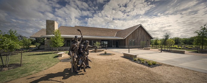 Panoramic view of a wooden museum building with a statue of an early Texas family in front