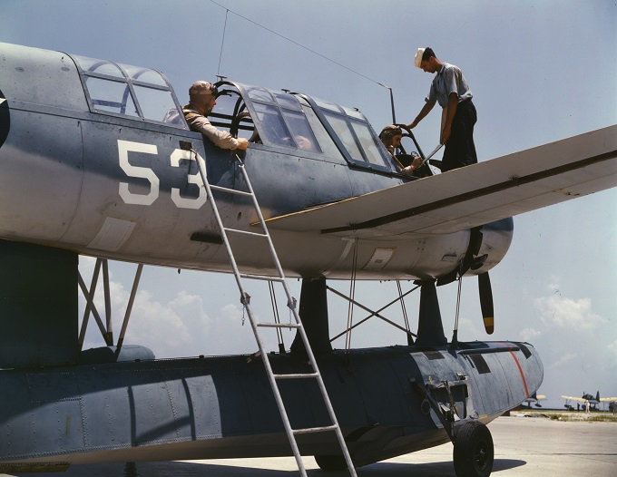 World War II seaplane with the number 53. A ladder leans against the side of the plane, where a cadet stands on the wing to talk to the two pilots in the cockpits.