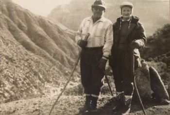 Two people with walking sticks on a hike in the mountains.