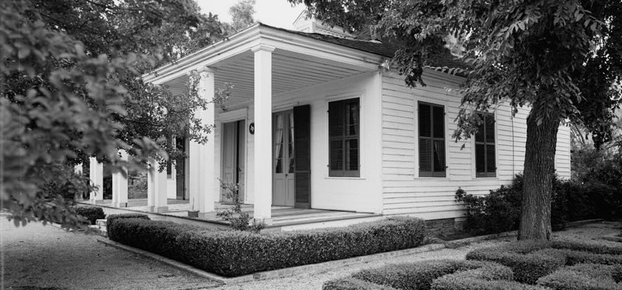 A black and white photo of the white columns of the French Legation building with tree branches in the foreground.