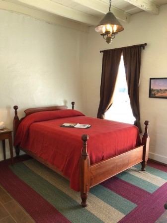 Queen size bed with red coverlet and next to a window