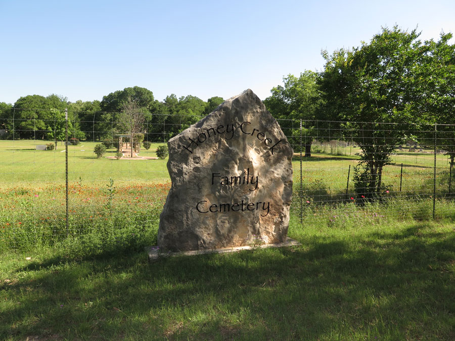 A photo of a large rock in a grass field inscribed with the words "Honey Creek Family Cemetery"
