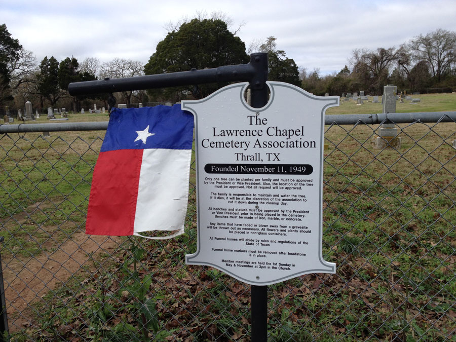 A white informational sign posted on the fence outside a family cemetery
