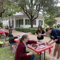 A group of people at the Texas Archeology Month Fair at the French Legation make pinch pots with other demonstrations in the background.