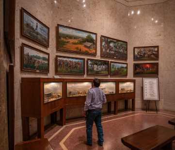A man stands in a room looking at paintings on the wall