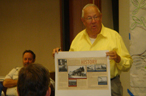 An older man holds up an information graphic before an audience
